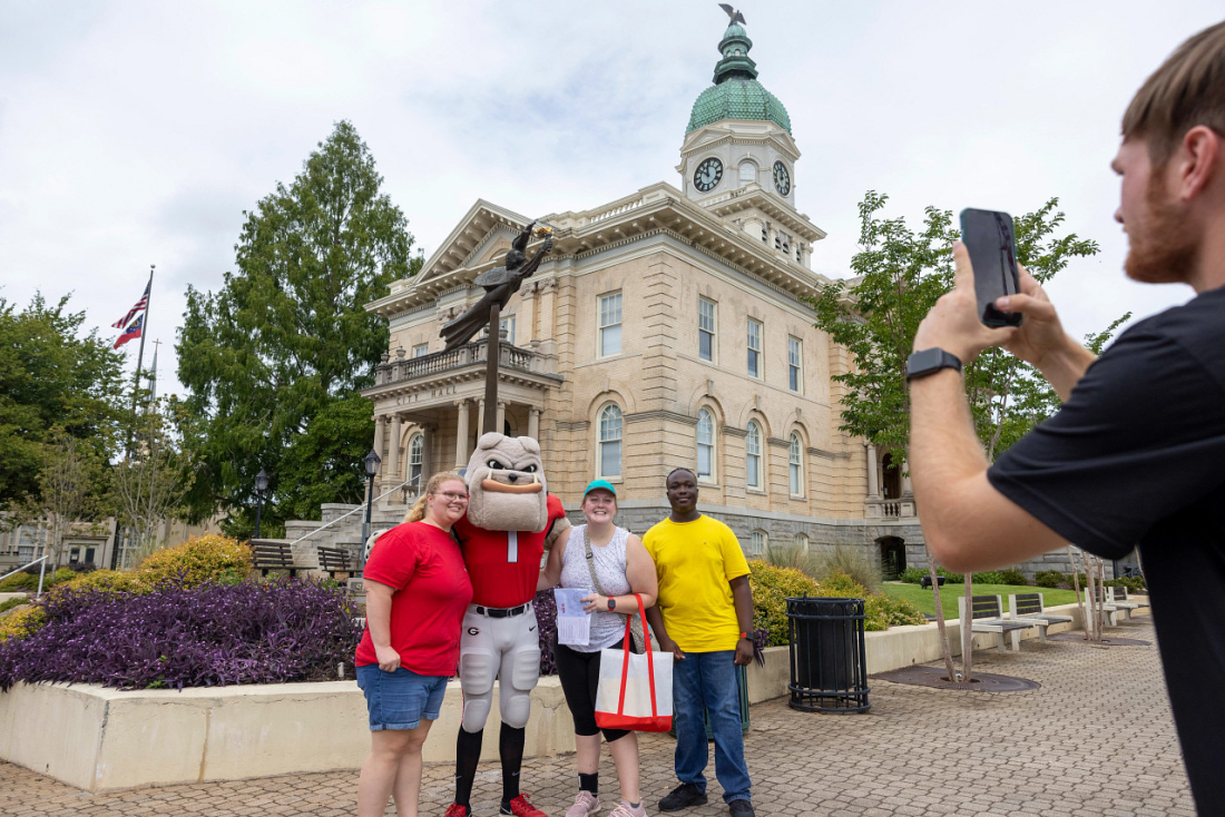 UGA's Hairy Dawg poses with guests while a man takes their photo.