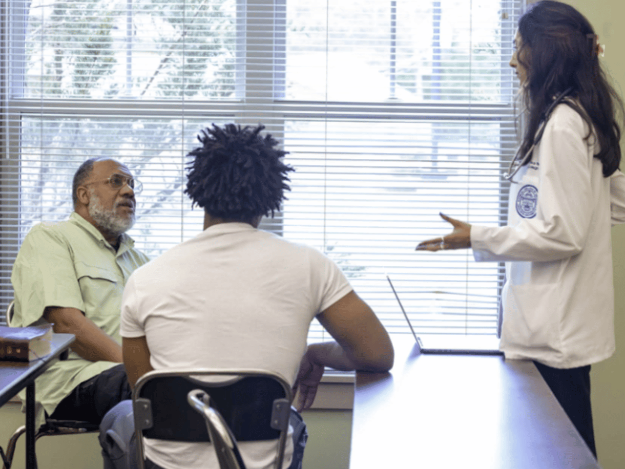 Two men speak with a UGA med student at the Athens Free Clinic.