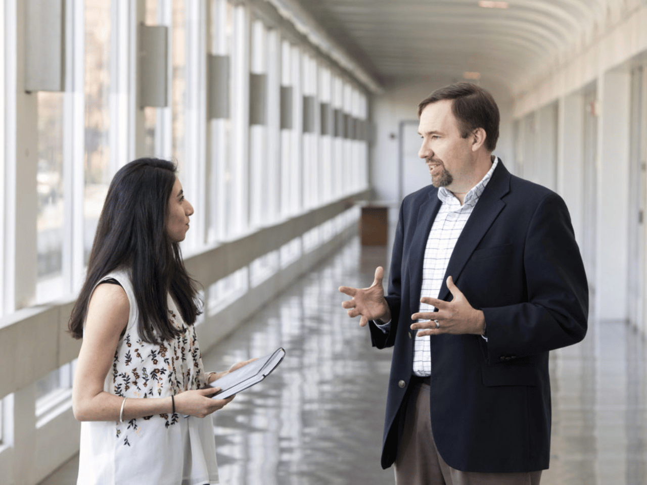 Two professionals talk in a hallway.